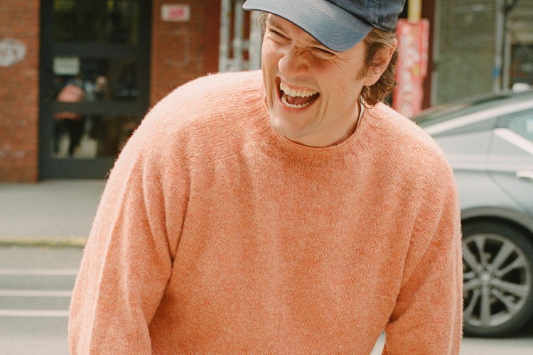 A man in a peach sweater with a New York Rangers baseball cap laughing, with the text "What's in Your Algo?" over the top