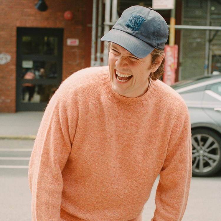 A man in a peach sweater with a New York Rangers baseball cap laughing, with the text "What's in Your Algo?" over the top