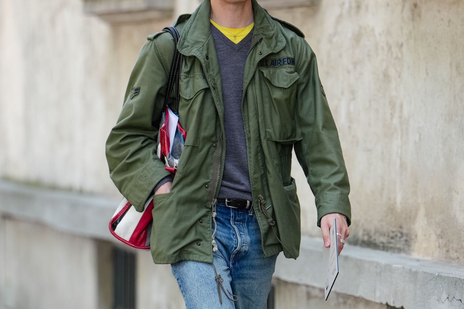 A man wearing dark yellow gray long sleeve sweater, dark green cargo jacket, navy blue ripped baggy denim jean pants, shiny black oxford moccasin leather shoes