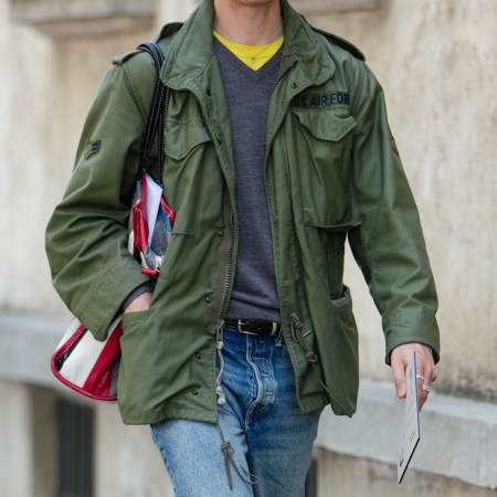 A man wearing dark yellow gray long sleeve sweater, dark green cargo jacket, navy blue ripped baggy denim jean pants, shiny black oxford moccasin leather shoes