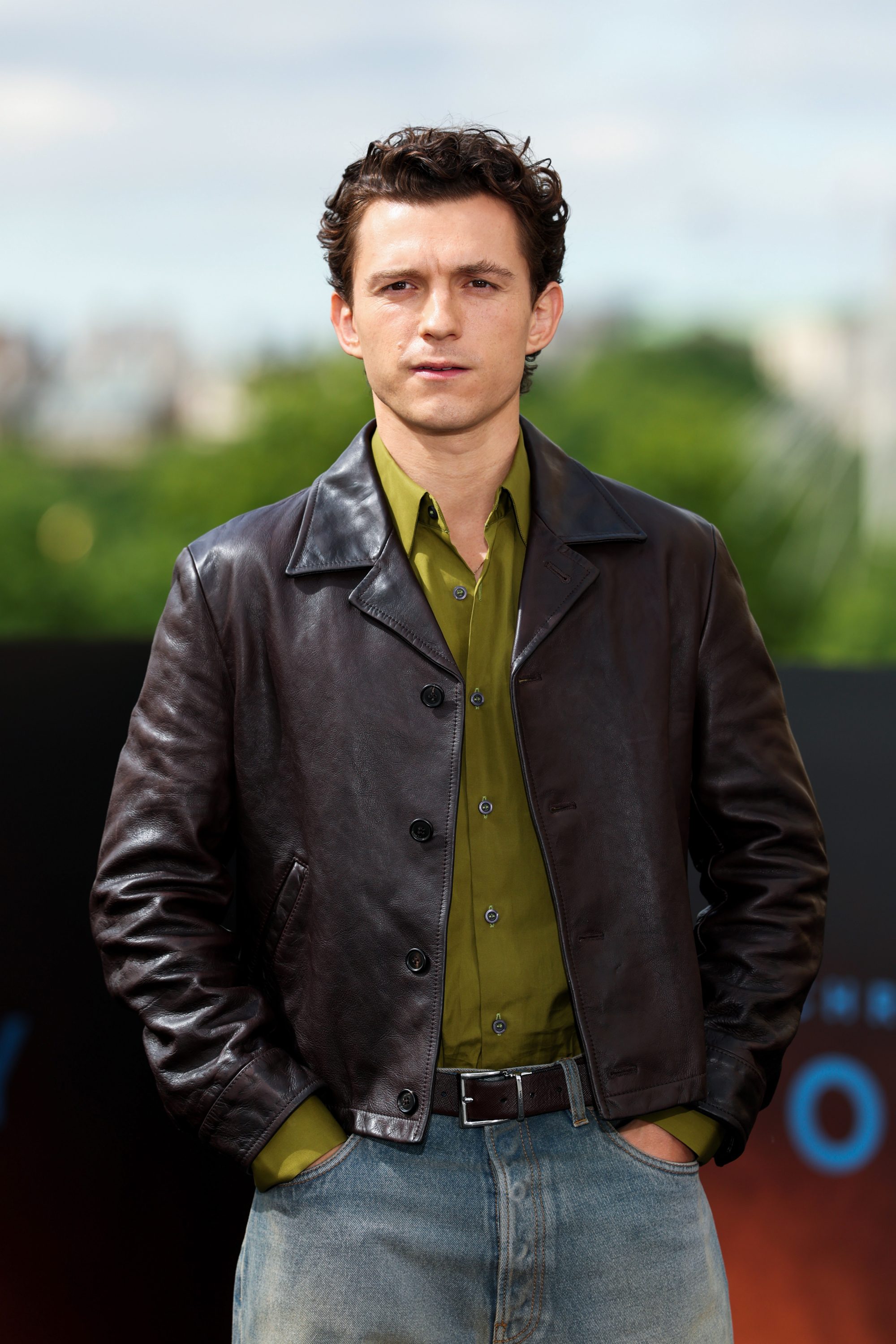A man in a leather jacket and green shirt standing for a photo.