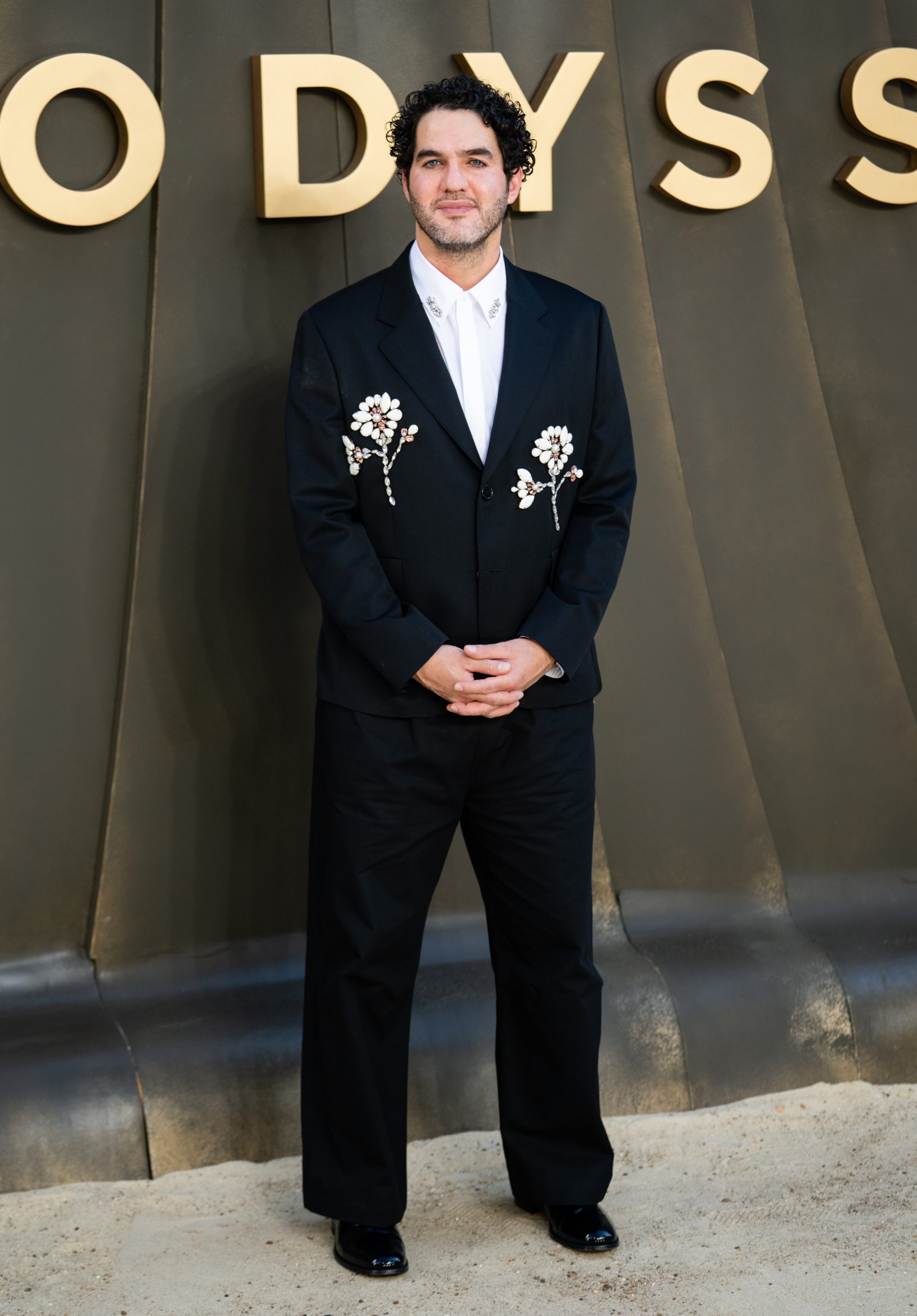 A man in a black suit with flower embroidery standing for a photo.