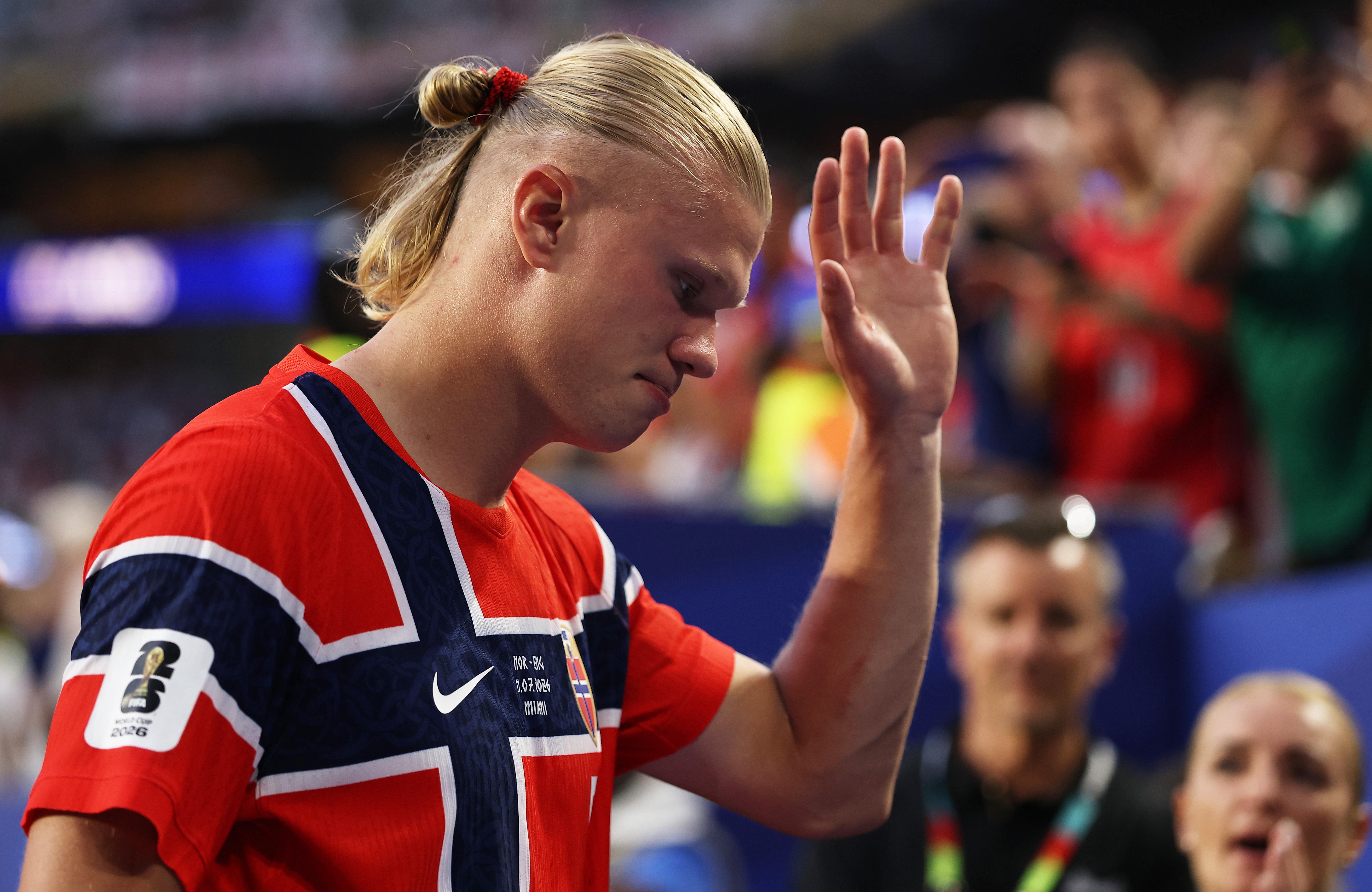 A blonde soccer player in a red jersey raising his left arm