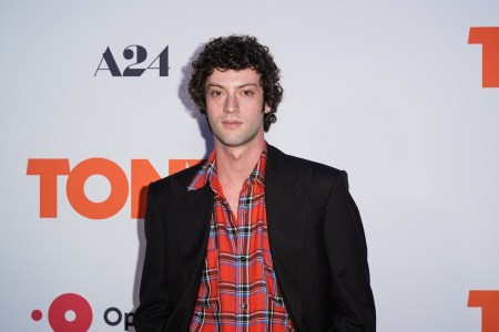 a man with curly black hair in a black suit and red plaid shirt
