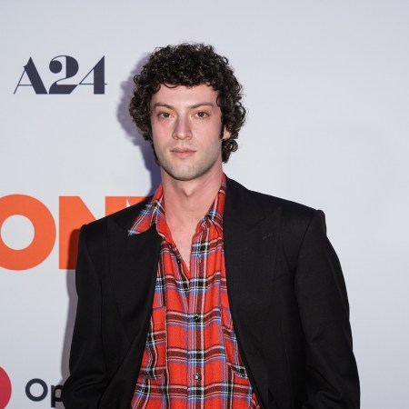 a man with curly black hair in a black suit and red plaid shirt
