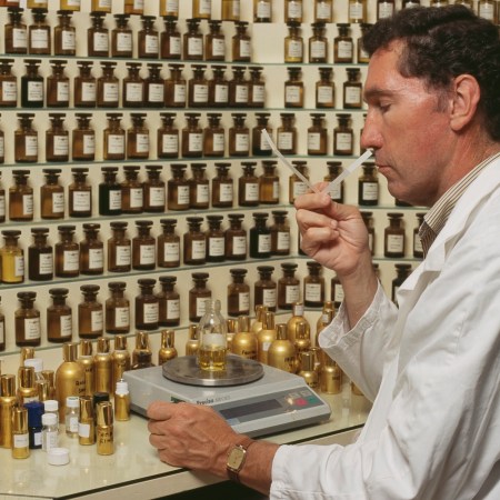 A man sniffing a stick inside a room filled with fragrance bottles