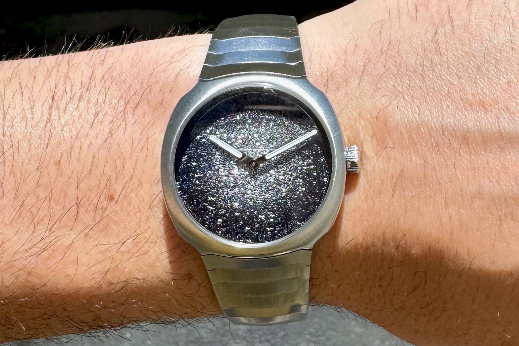 A stainless steel watch with two hands and a sparkling silver dial shown on a white man's wrist