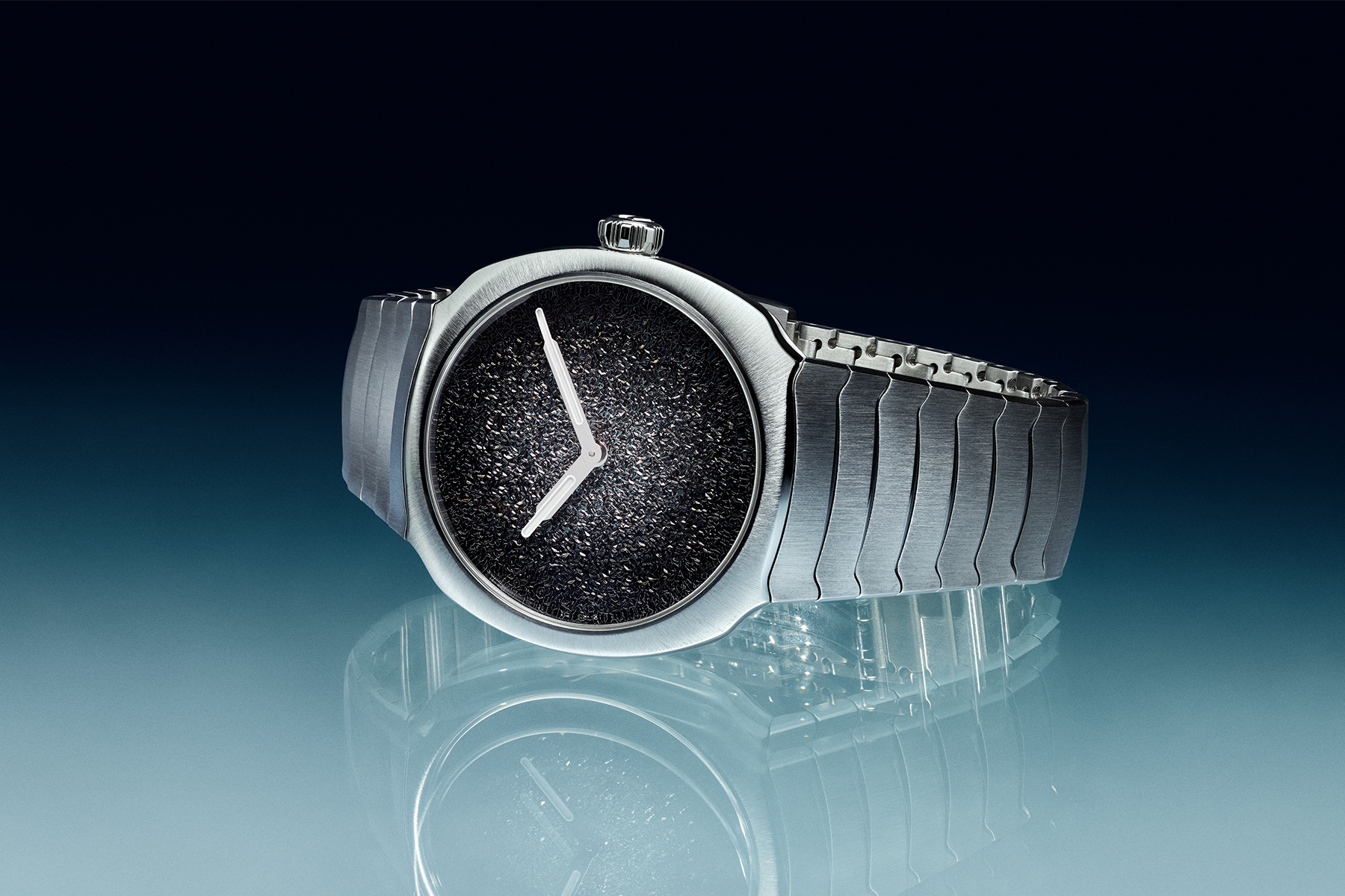 A stainless steel watch with two hands and a silver dial that fades from dark to light on a black and blue background
