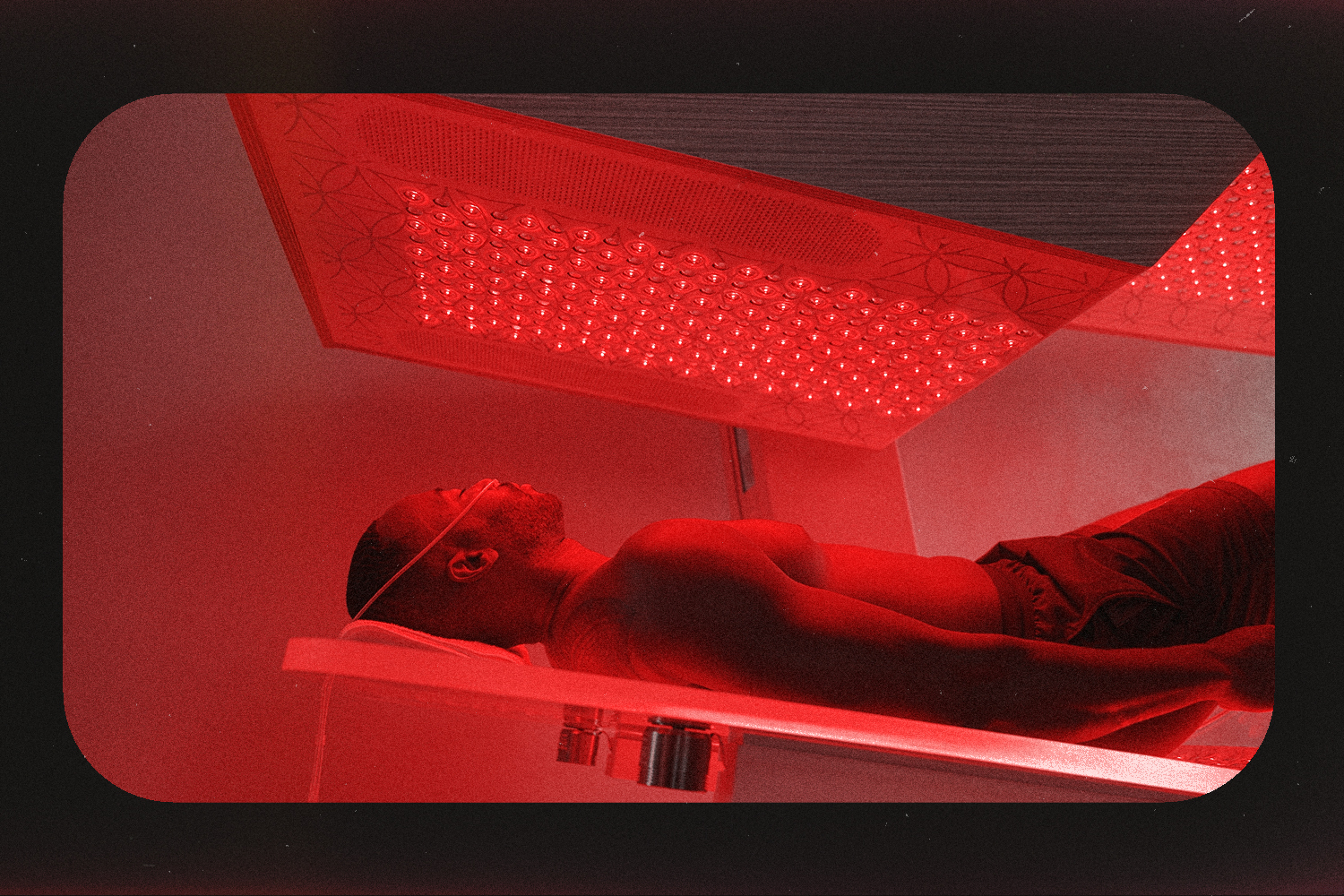 A man on an acrylic glass bed under a red-light panel.