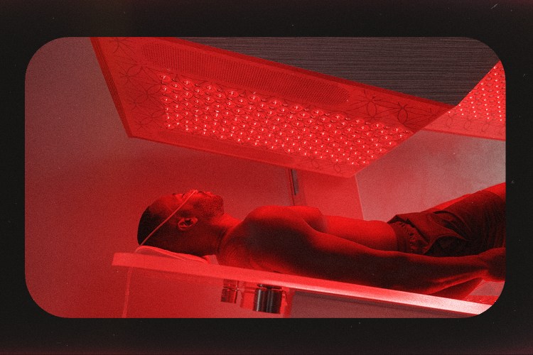 A man on an acrylic glass bed under a red-light panel.