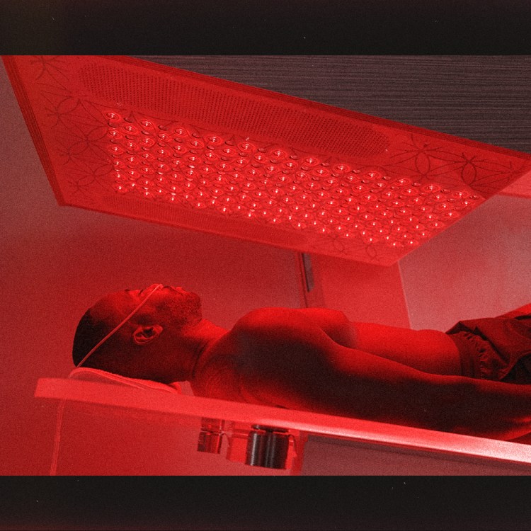 A man on an acrylic glass bed under a red-light panel.