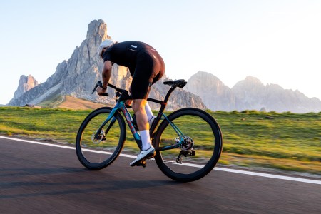 A man riding a bike down the road in lycra gear, shown from the back, with rock formations in the background