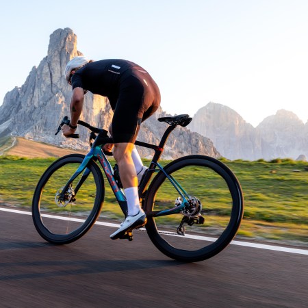 A man riding a bike down the road in lycra gear, shown from the back, with rock formations in the background