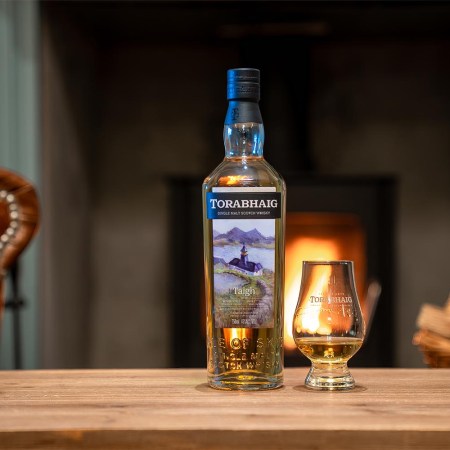 A bottle of Torabhaig Taigh whiskey and a glass of whiskey on a table indoors