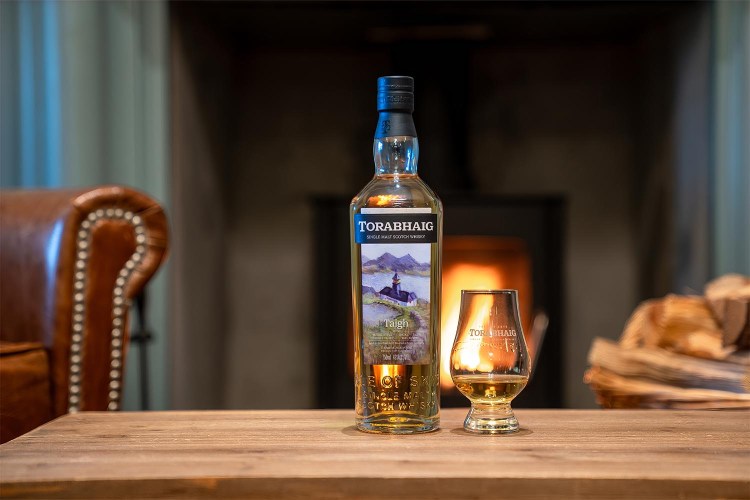 A bottle of Torabhaig Taigh whiskey and a glass of whiskey on a table indoors