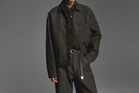 A model in a dark wash Uniqlo denim trucker jacket and jeans set against a grey background