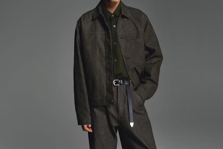 A model in a dark wash Uniqlo denim trucker jacket and jeans set against a grey background