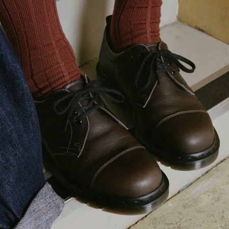 A pair of brown leather derby shoes being worn with orange-brown socks next to someone wearing jeans