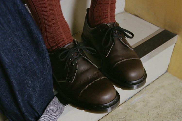 A pair of brown leather derby shoes being worn with orange-brown socks next to someone wearing jeans