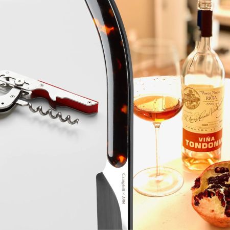 A wine key with a red handle on the left, a Champagne saber in the middle, and on the right a table with a bottle of wine, a wine glass and a pomegranate cut in half to show the seeds
