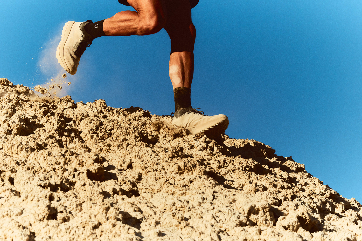 Man running on sandy dune in beige running shoes.