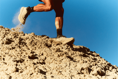 Man running on sandy dune in beige running shoes.