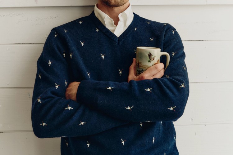a model in a white button down under a navy embroidered sweater