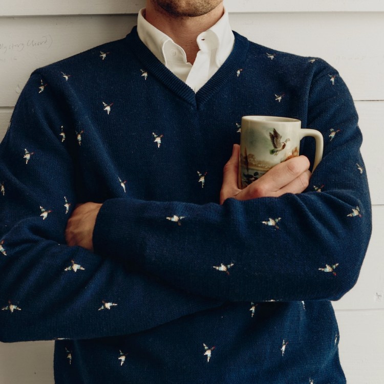 a model in a white button down under a navy embroidered sweater