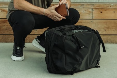 a model holding a leather wallet squatting by a black Patagonia bag.