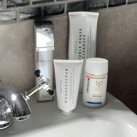Skincare products on a bathroom sink: a silver bottle, two white tubes, and a white bottle of SPF 50.