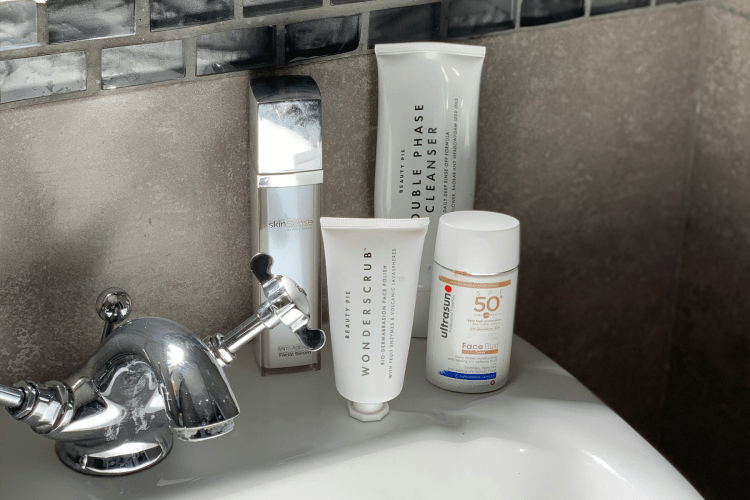 Skincare products on a bathroom sink: a silver bottle, two white tubes, and a white bottle of SPF 50.