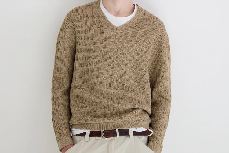 a model in a tan sweater over a white t-shirt against a white wall