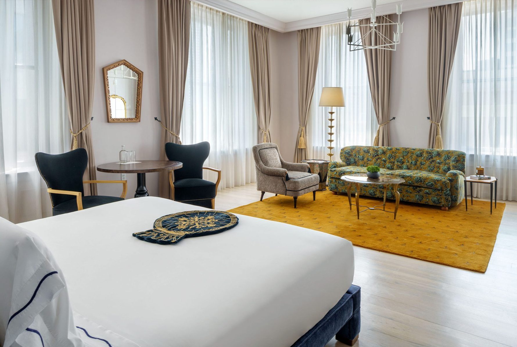 a hotel room with a seating area with yellow rug, two chairs and a small table and a king-sized bed