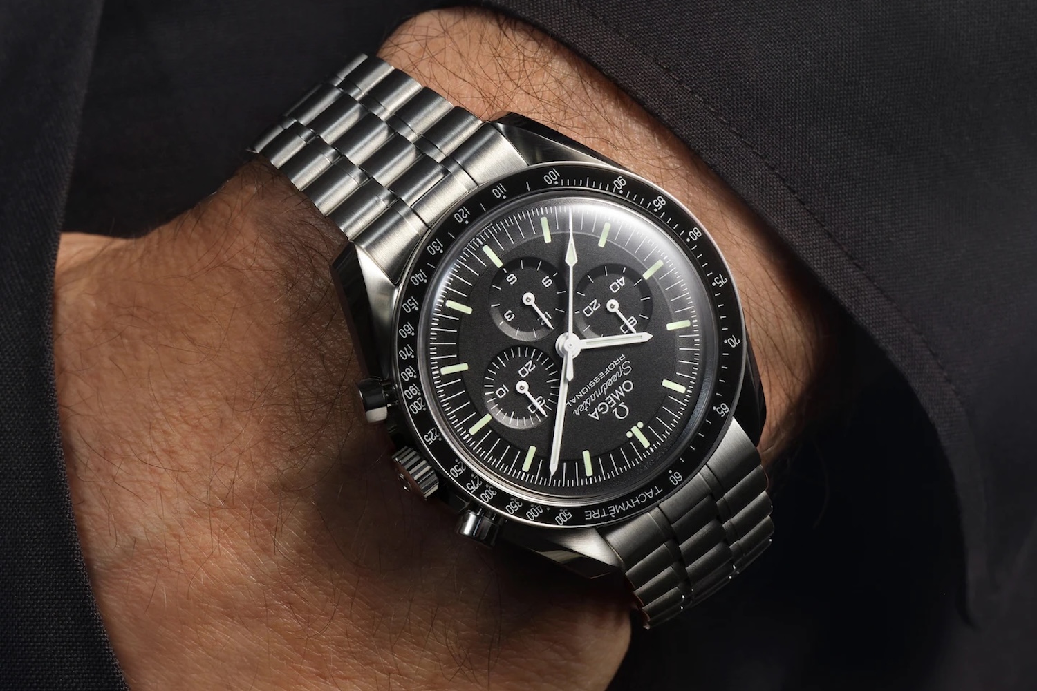 A man's wrist wearing an Omega Speedmaster Professional watch with a black dial and steel bracelet.