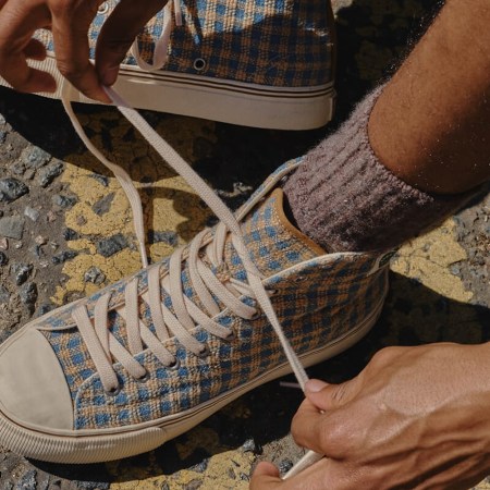 A model tying a pair of brown checked high-top sneakers.