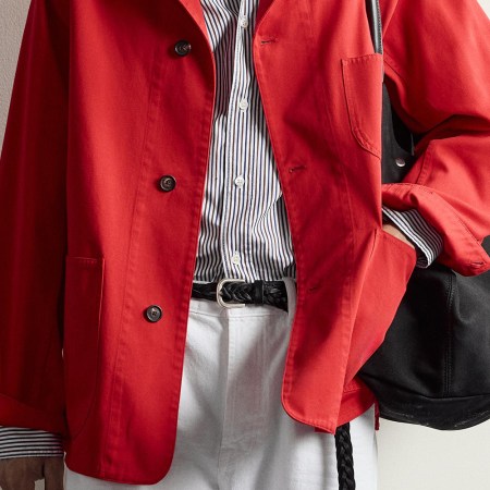 a model in a red coat, striped shirt and white pants