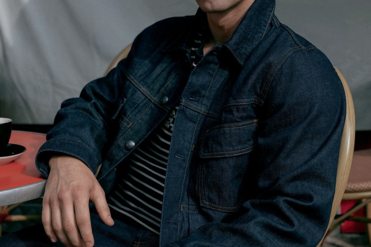 Person in a dark denim jacket and striped shirt, seated at a red table with a coffee cup.