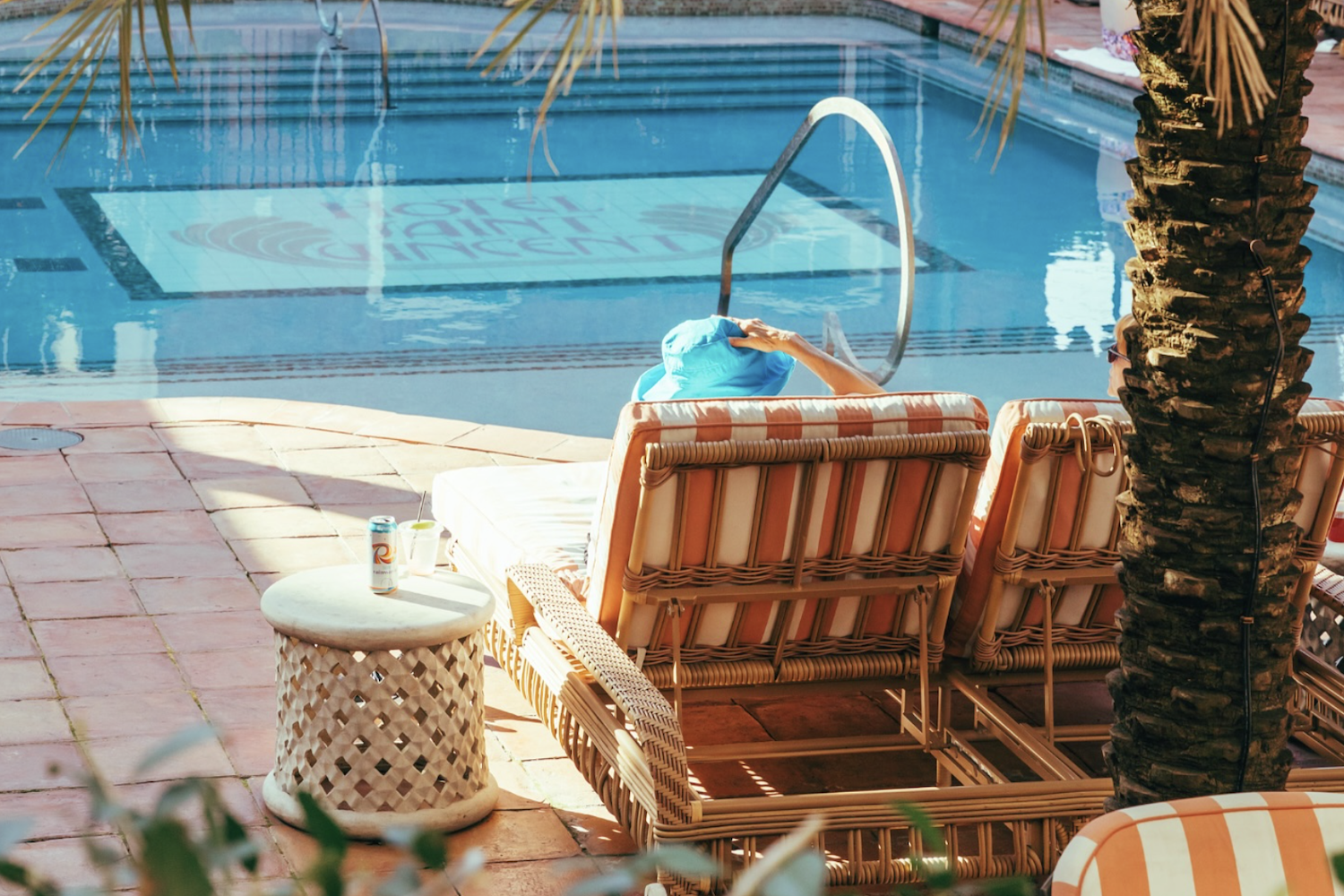Person in a blue hat relaxing on a striped lounge chair by a pool with "Hotel Saint Vincent" visible at the bottom.