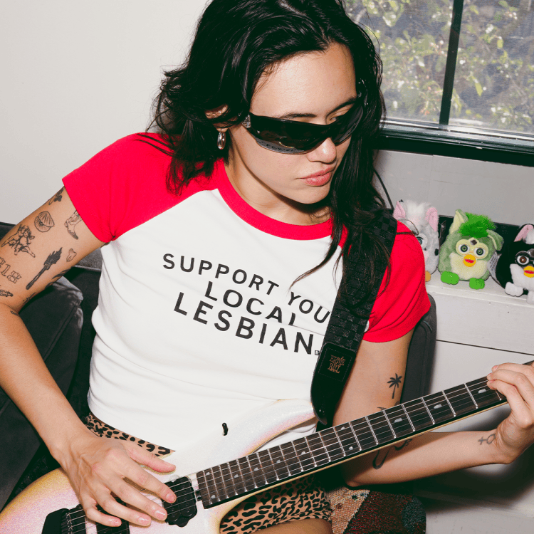 rivkah reyes wearing sunglasses playing a guitar with furbies in the background