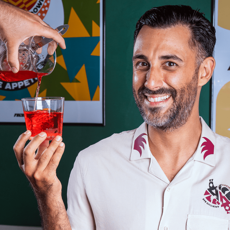 a man with a short beard and dark hair in a white shirt holding a negroni