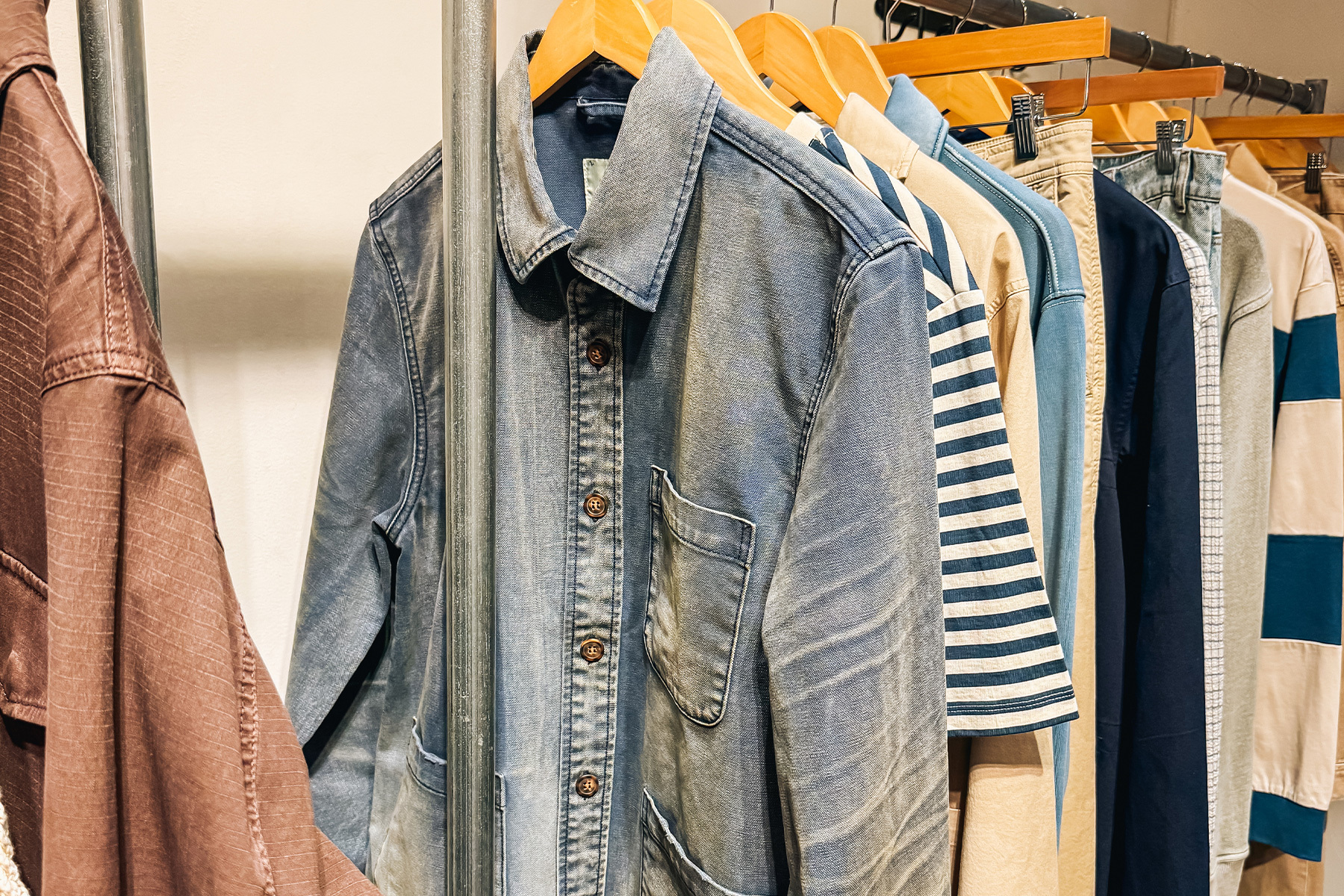 A clothing rack with various shirts, including a faded blue denim shirt, striped shirt, and other casual wear.