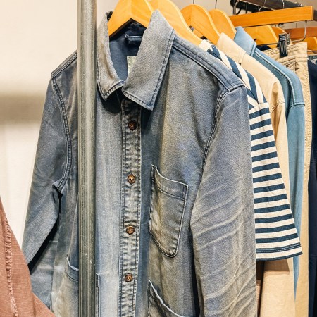 A clothing rack with various shirts, including a faded blue denim shirt, striped shirt, and other casual wear.
