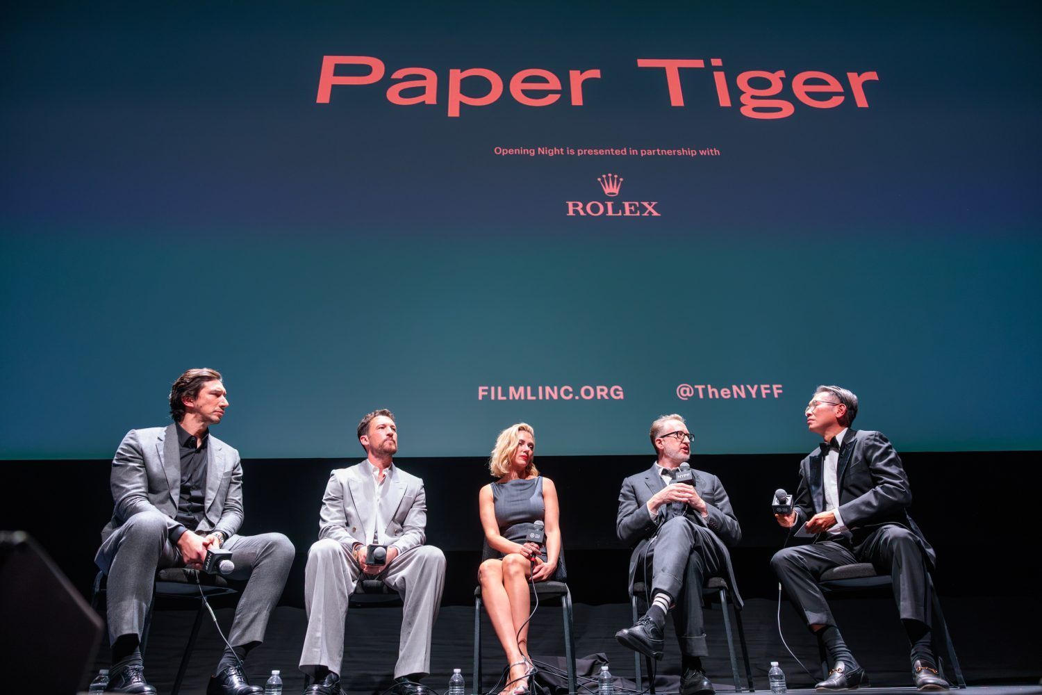 Five panelists, including Adam Driver and Scarlett Johansson, sit on stage with microphones, facing a screen that reads "Paper Tiger."