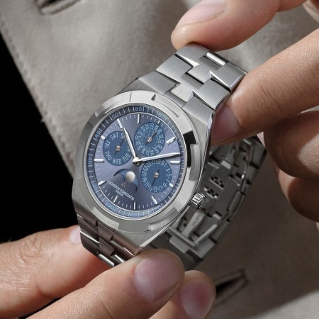 Hands adjust a Vacheron Constantin Overseas Perpetual Calendar Ultra-Thin watch with a blue dial and steel bracelet.