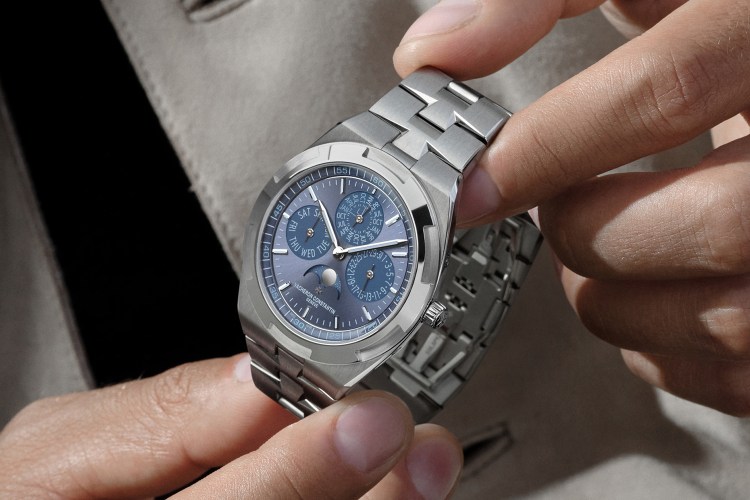 Hands adjust a Vacheron Constantin Overseas Perpetual Calendar Ultra-Thin watch with a blue dial and steel bracelet.