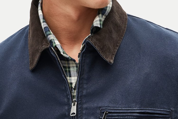Close-up of a person wearing a navy blue jacket with a brown corduroy collar over a green and white plaid shirt.