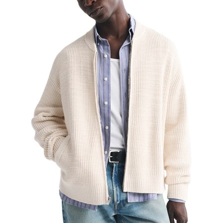 Man in a cream ribbed knit zip-up cardigan over a blue striped shirt, white undershirt, and light wash jeans.