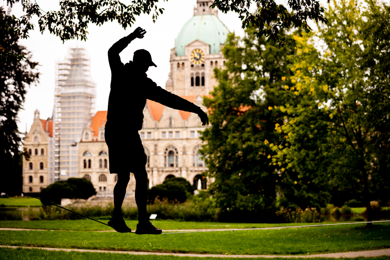 Silhouette of a person slacklining in a park with a large domed building in the background.